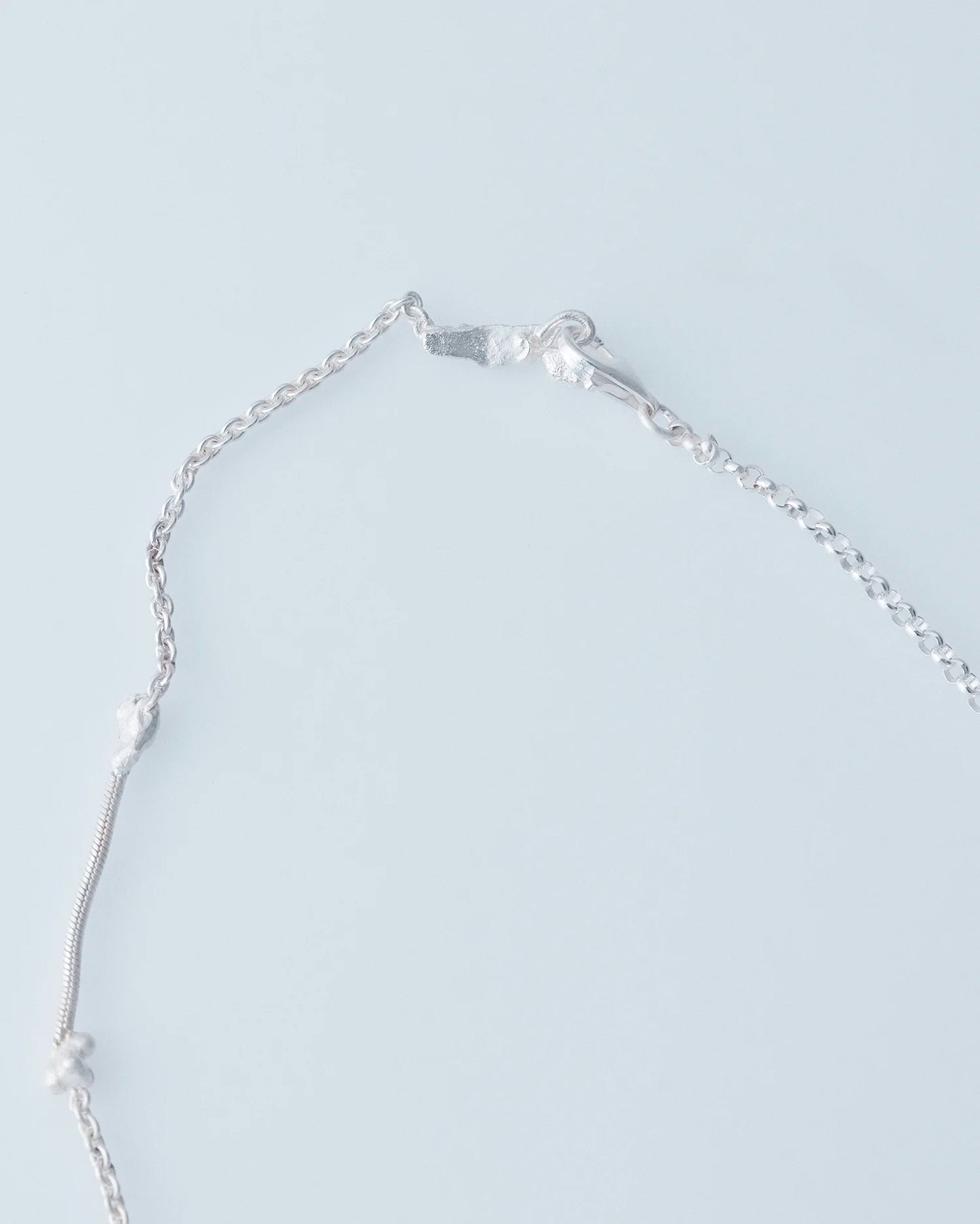 Silver necklace with a chain on a light gray background