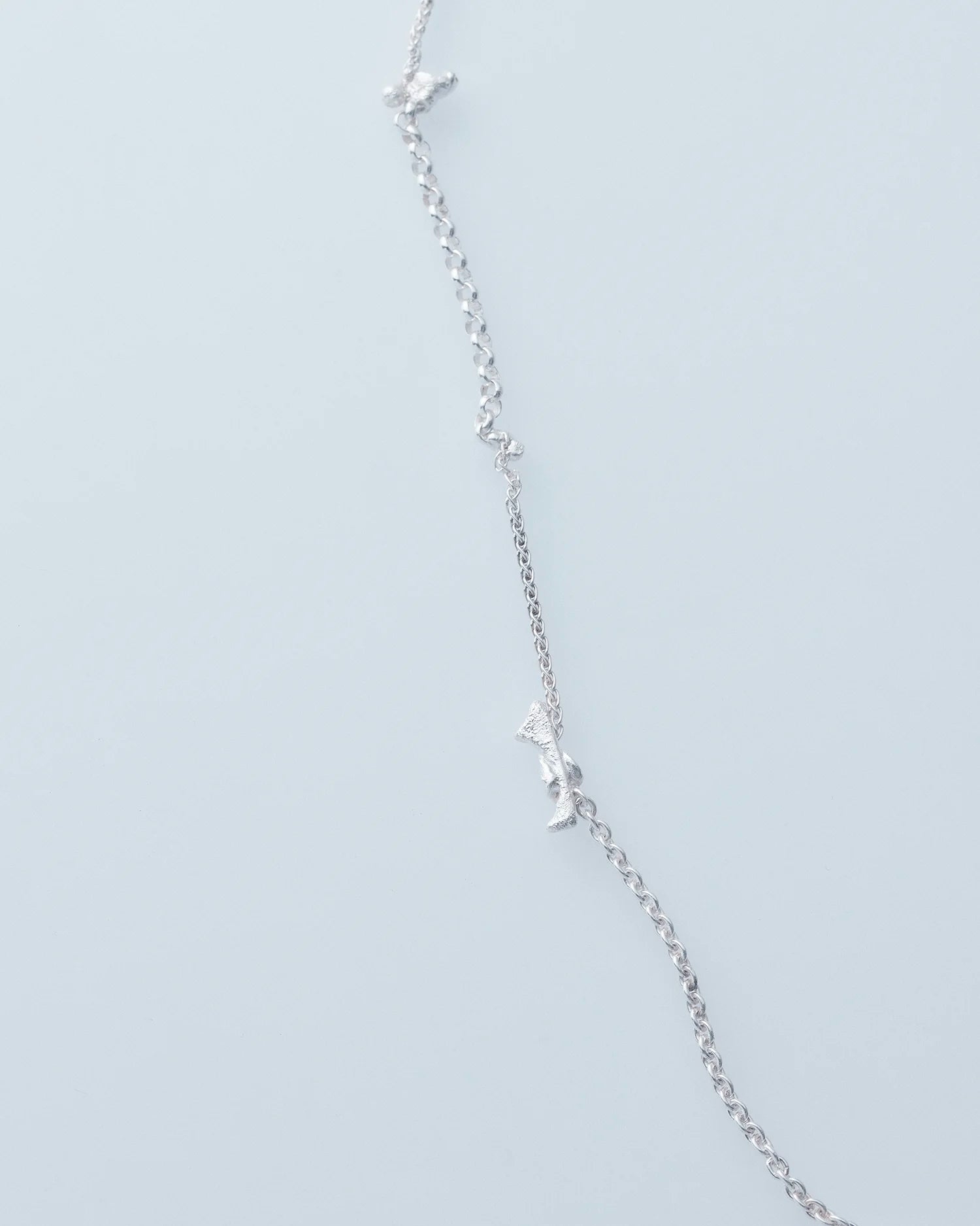 Silver necklace with small star-shaped pendants on a light gray background